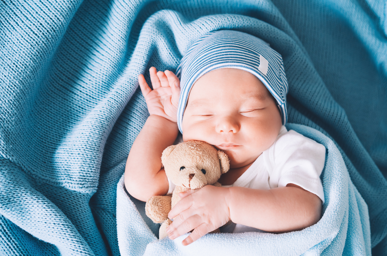 Infant wrapped in blue blanket holding teddy bear