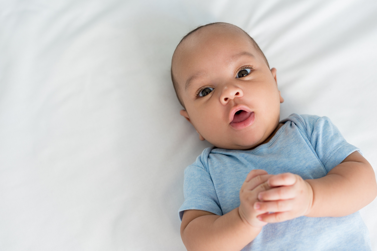Baby wearing a blue onesie lying on a white sheet