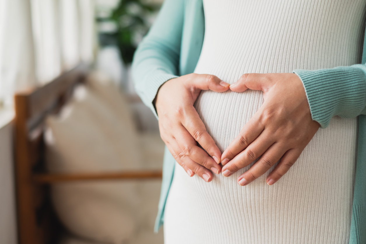 Woman holds hands in heart shape on pregnant belly