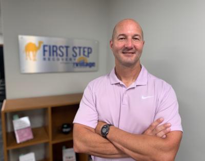 Thad Stafford standing with arms crossed in front of First Step Recovery sign