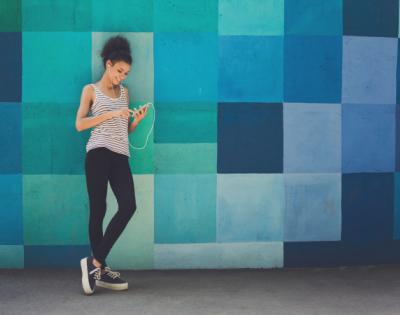 Girl standing against colorful wall with headphones looking at her phone