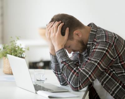 Man sitting at a computer with head in hands looking distressed