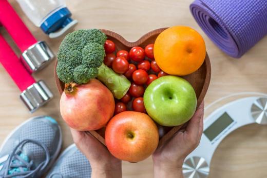 Heart-shaped bowl of fruit and vegetables surrounded by exercise equipment