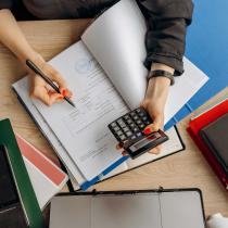 A person's hands hold a calculator and jot down numbers
