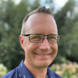Headshot of Patrick Schultz, a white man with glasses wearing a blue top