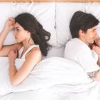Unhappy couple laying in bed facing away from each other