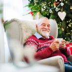 Elderly man sitting in front of Christmas tree with cup of coffee smiling