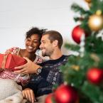Couple sitting by Christmas tree exchanging a gift