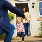 Child running to father with mother standing and smiling in the house doorway behind the child.