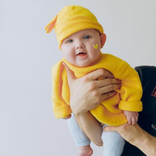 Baby in bright yellow hat and sweater with heart of face