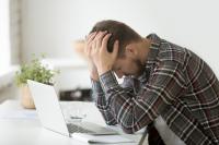Man sitting at a computer with head in hands looking distressed