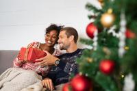 Couple sitting by Christmas tree exchanging a gift